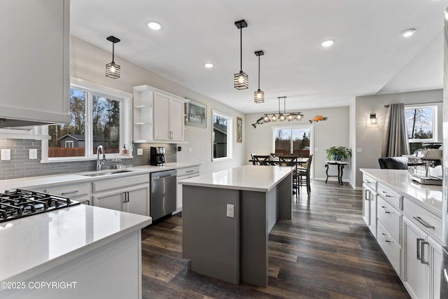 kitchen featuring stainless steel dishwasher, decorative light fixtures, a kitchen island, backsplash, and a sink