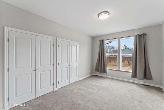 unfurnished bedroom featuring visible vents, two closets, carpet, and baseboards