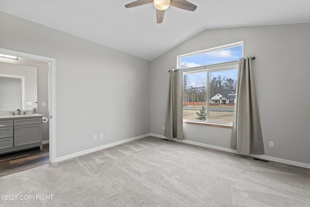 unfurnished bedroom featuring connected bathroom, carpet, vaulted ceiling, a sink, and baseboards