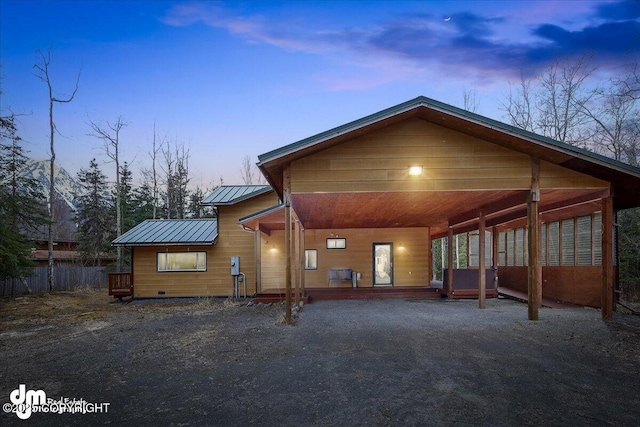back of property at dusk with covered porch, a standing seam roof, driveway, metal roof, and an attached carport