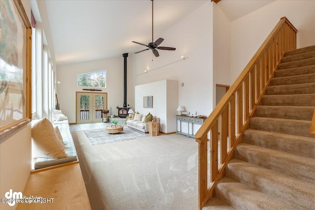 carpeted living area featuring ceiling fan, a wood stove, high vaulted ceiling, baseboards, and stairway