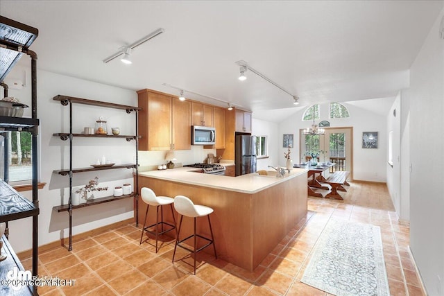 kitchen with track lighting, a peninsula, light countertops, light tile patterned floors, and stainless steel appliances