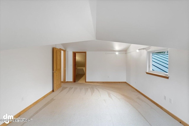 spare room featuring baseboards, light colored carpet, and lofted ceiling