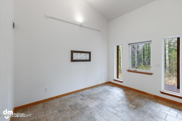 spare room featuring baseboards, stone finish floor, and vaulted ceiling