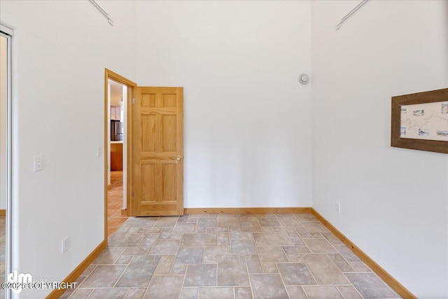empty room with baseboards, a towering ceiling, and stone finish floor