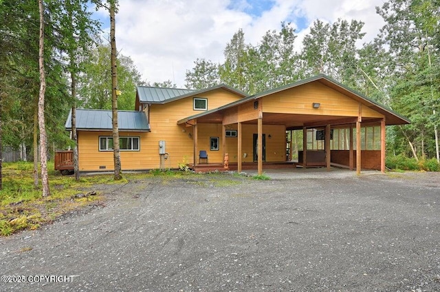 chalet / cabin with a deck, an attached carport, a standing seam roof, metal roof, and driveway