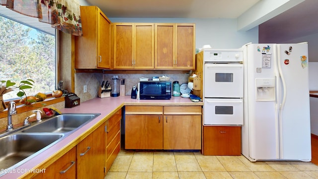 kitchen featuring a sink, brown cabinets, white appliances, light tile patterned floors, and backsplash