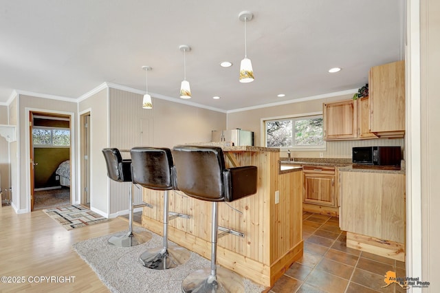 kitchen featuring black microwave, a kitchen bar, freestanding refrigerator, ornamental molding, and light brown cabinets