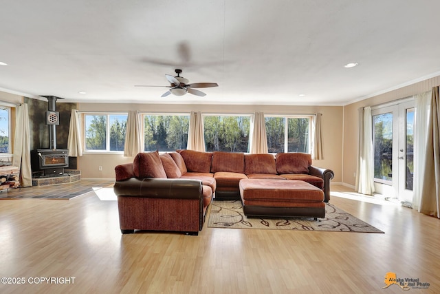 living room with light wood-type flooring, crown molding, a wood stove, a ceiling fan, and baseboards