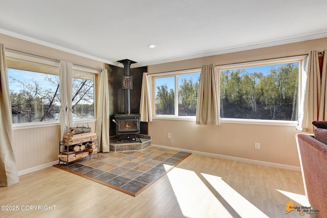 living room featuring wood finished floors, plenty of natural light, a wood stove, and ornamental molding