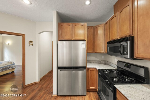 3600 N Fortune Cir, Wasilla, AK 99654 - kitchen with stainless steel appliances, wood finished floors, light stone countertops, a textured ceiling, and arched walkways