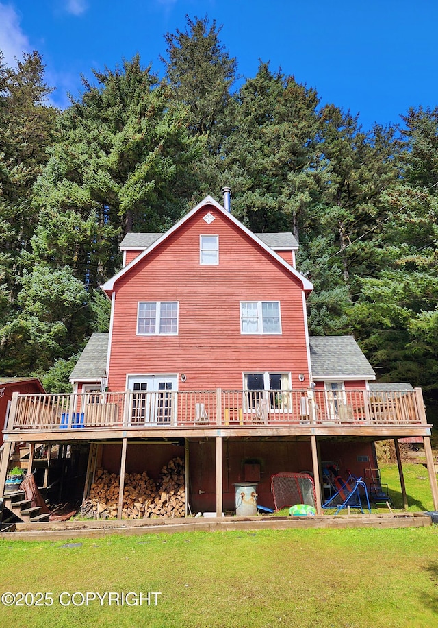 rear view of house with a wooden deck, a lawn, and a wooded view