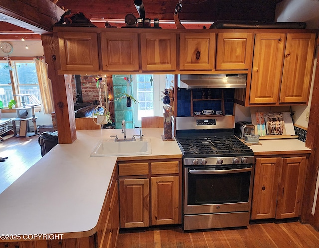 kitchen with stainless steel range with gas cooktop, brown cabinets, under cabinet range hood, and a sink