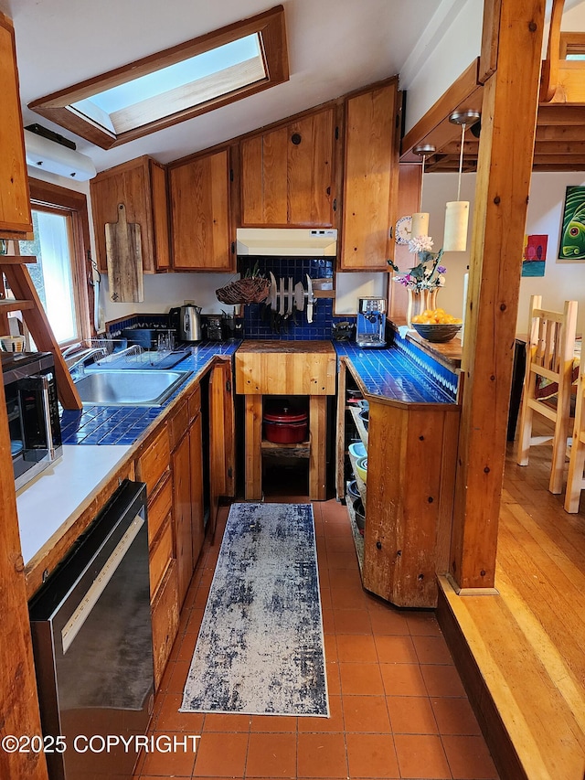 kitchen with brown cabinetry, stainless steel microwave, a sink, and dishwashing machine