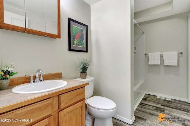 bathroom featuring toilet, wood finished floors, shower / washtub combination, vanity, and baseboards