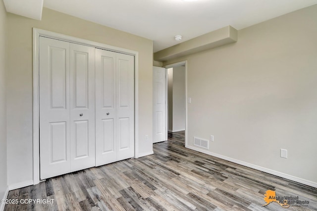 unfurnished bedroom featuring wood finished floors, a closet, and baseboards