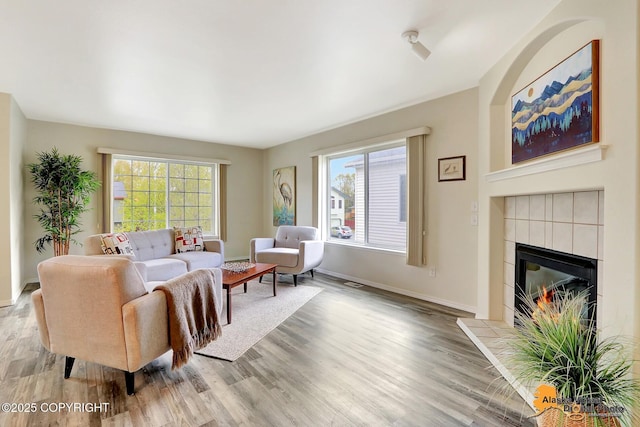 living room featuring wood finished floors, a tile fireplace, and baseboards