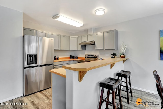 kitchen featuring stainless steel appliances, gray cabinets, a peninsula, a kitchen breakfast bar, and under cabinet range hood