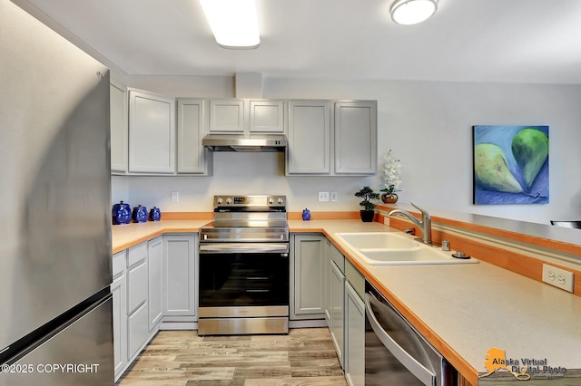 kitchen with appliances with stainless steel finishes, a sink, light countertops, light wood-type flooring, and a peninsula