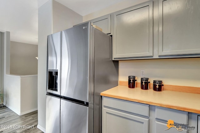 kitchen with stainless steel fridge, light wood-type flooring, light countertops, and gray cabinets