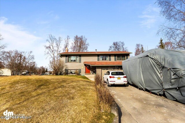 split foyer home featuring a garage, a chimney, a front yard, and concrete driveway