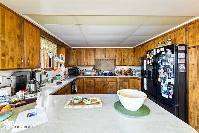 kitchen featuring a paneled ceiling, a sink, brown cabinetry, light countertops, and black appliances