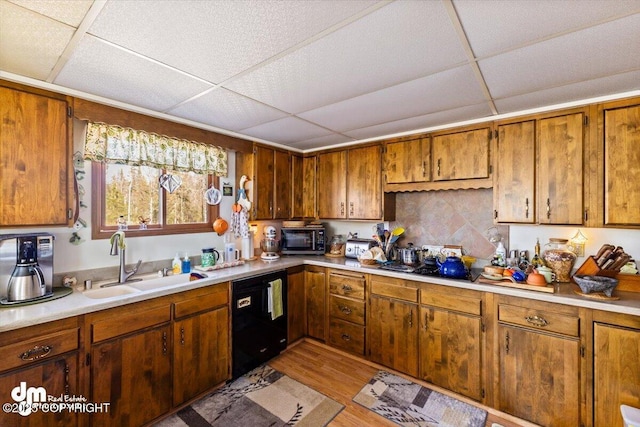 kitchen with a paneled ceiling, a sink, black dishwasher, brown cabinets, and light countertops