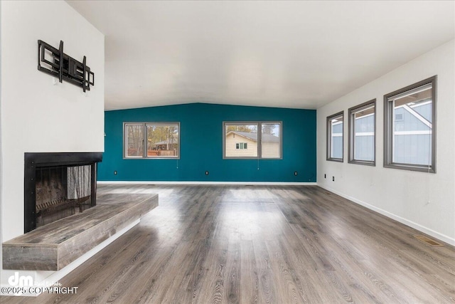 unfurnished living room featuring baseboards, a fireplace with raised hearth, wood finished floors, and lofted ceiling
