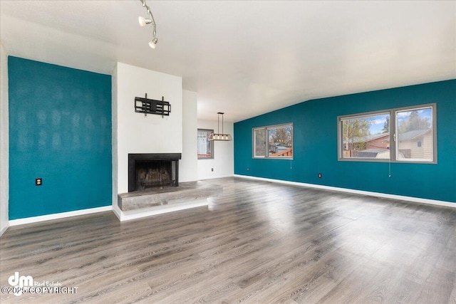 unfurnished living room with a fireplace with raised hearth, baseboards, and wood finished floors