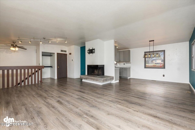 unfurnished living room featuring visible vents, a ceiling fan, a multi sided fireplace, and wood finished floors