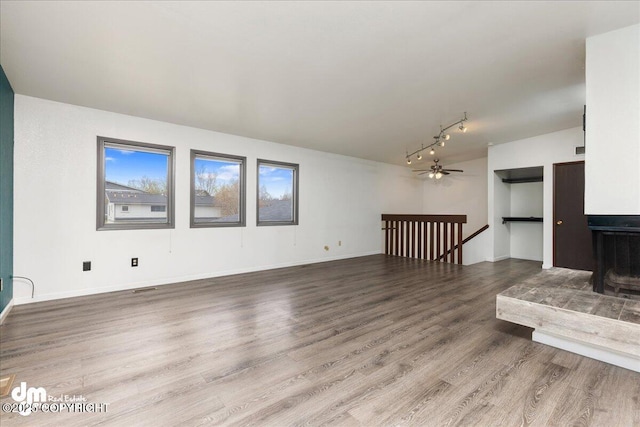 unfurnished living room with visible vents, rail lighting, baseboards, and wood finished floors