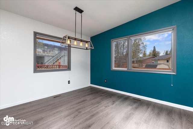 unfurnished room featuring baseboards, visible vents, and wood finished floors