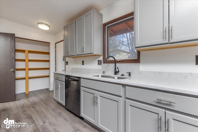 kitchen with light stone countertops, dishwasher, a sink, gray cabinetry, and light wood-style floors