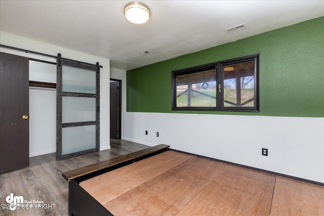 unfurnished bedroom featuring visible vents, a barn door, baseboards, and wood finished floors