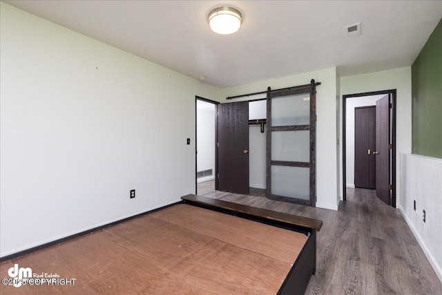 unfurnished bedroom with baseboards, visible vents, a barn door, and wood finished floors