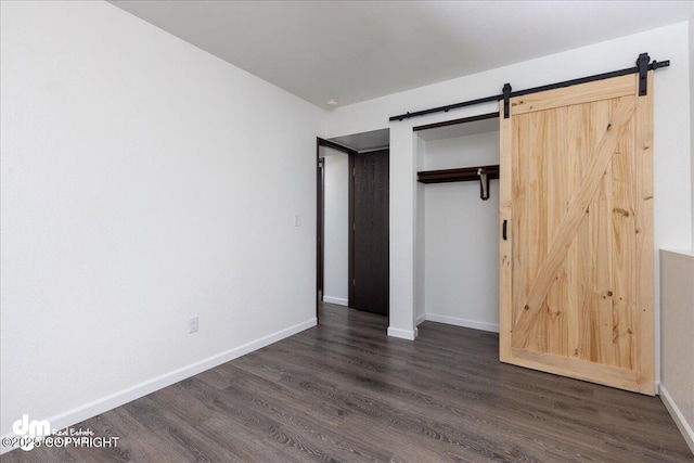 unfurnished bedroom featuring baseboards, a barn door, dark wood-style floors, and a closet