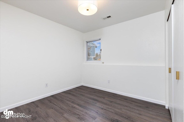 unfurnished room with baseboards, visible vents, and dark wood-style floors