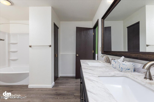 bathroom featuring baseboards, a sink, wood finished floors, and double vanity
