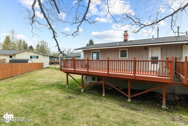back of property with a chimney, roof with shingles, a deck, fence, and a yard