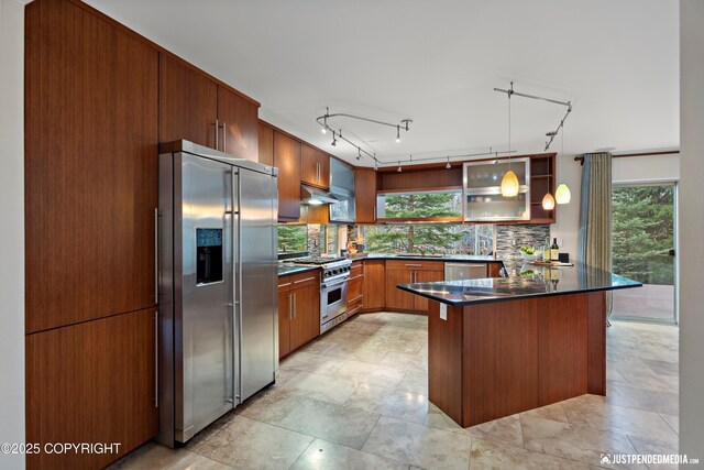kitchen featuring decorative backsplash, dark countertops, a peninsula, premium appliances, and under cabinet range hood