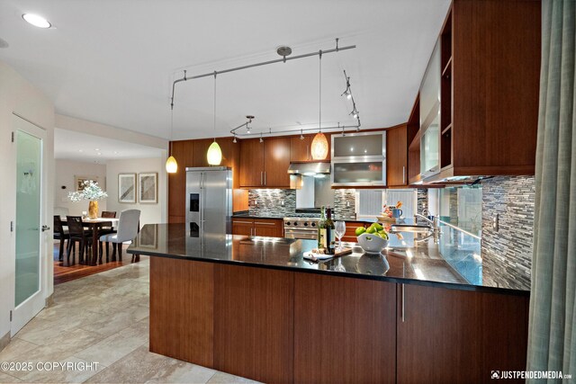 kitchen with a peninsula, decorative light fixtures, high end appliances, tasteful backsplash, and under cabinet range hood