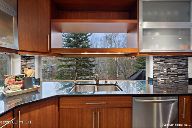 kitchen with stainless steel dishwasher, brown cabinetry, dark stone counters, tasteful backsplash, and a sink