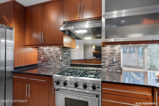 kitchen with under cabinet range hood, appliances with stainless steel finishes, dark stone counters, and tasteful backsplash
