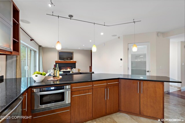 kitchen with pendant lighting, open floor plan, a warm lit fireplace, dark stone countertops, and stainless steel appliances