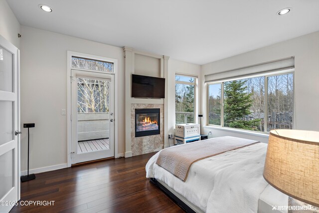 bedroom with a glass covered fireplace, baseboards, recessed lighting, and wood finished floors