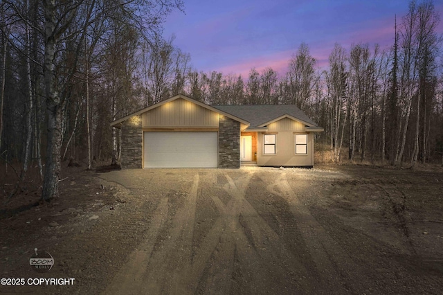 7177 N Paw St, Wasilla, AK 99654 - view of front of house with dirt driveway, an attached garage, and stone siding