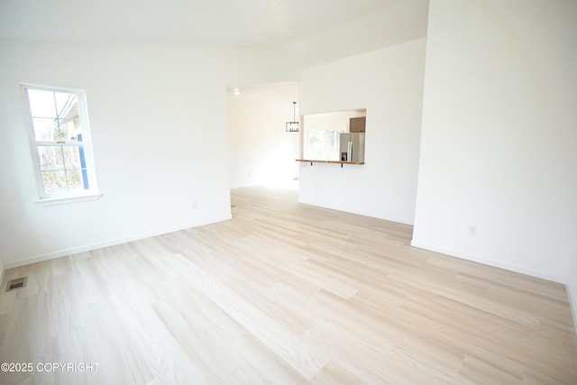 spare room with visible vents, light wood finished floors, baseboards, and vaulted ceiling