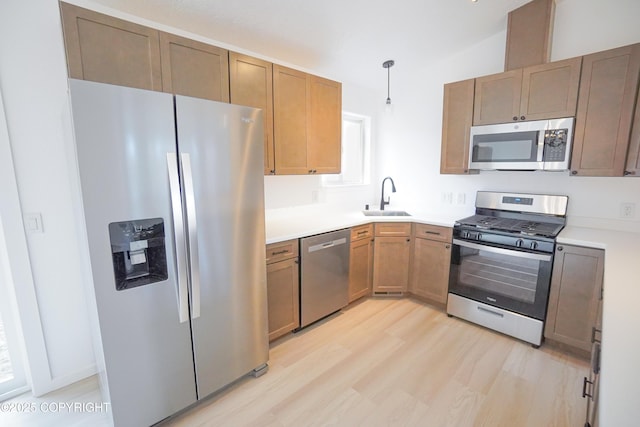 kitchen featuring hanging light fixtures, a sink, light wood finished floors, light countertops, and stainless steel appliances