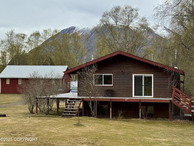 rear view of property with a yard, a deck with mountain view, and stairs