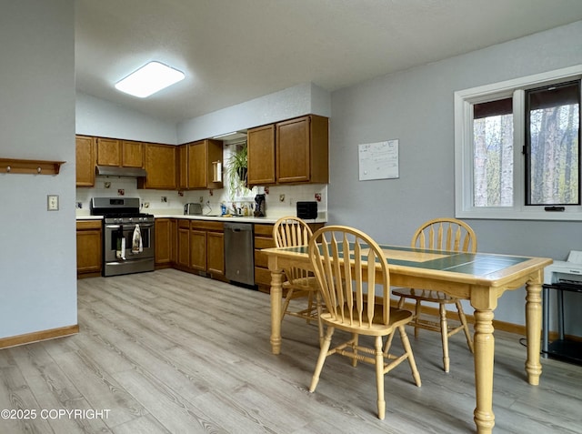 kitchen with appliances with stainless steel finishes, brown cabinets, baseboards, light wood finished floors, and lofted ceiling